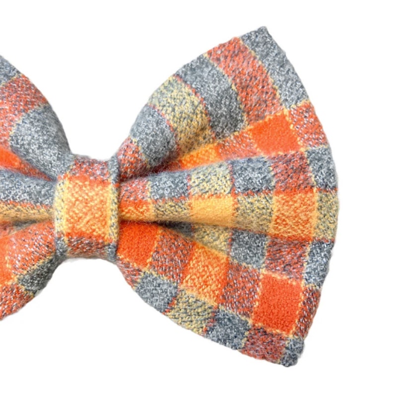 Plaid bow tie has a small check design. Stripes of orange and yellow lay on a light blue gray.