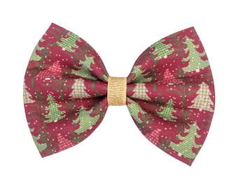 May include: A festive Christmas-themed bow tie. The bow tie features a burgundy background with a pattern of green and white Christmas trees. The center knot is a gold color.