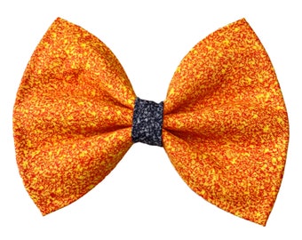 May include: A large orange and yellow bow with a black center. The bow is made of a sparkly fabric.