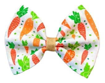 May include: A white fabric bow with a carrot print. The bow is tied with a brown ribbon.