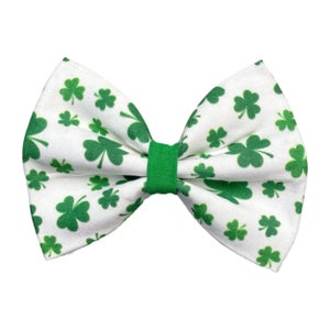 May include: A white bow tie with a green shamrock pattern. The bow tie is tied with a green ribbon.
