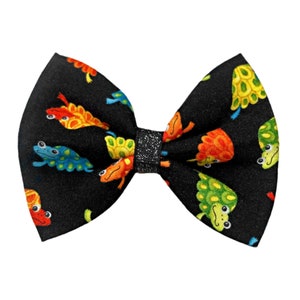 May include: A black bow tie with a glittery centre, featuring a repeating pattern of colourful frogs on a black background.