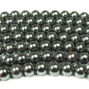 May include: Strands of polished, round, black hematite beads. The beads have a high-gloss finish, reflecting light. These beads are strung together, suitable for jewelry making. The beads are approximately 8mm in diameter.