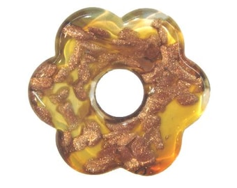 May include: A flower-shaped pendant with a central hole. The pendant is made of clear glass with a yellow and amber hue. Copper-colored glitter is embedded throughout the glass, creating a sparkling effect. The edges of the pendant are rounded.