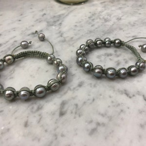 May include: Two gray pearl bracelets with green string ties. The bracelets are made of round pearls and are tied with a simple knot.