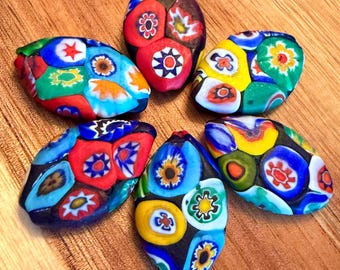 May include: Six oval-shaped glass beads featuring intricate millefiori patterns. Each bead displays a vibrant array of colors including red, blue, yellow, green, and white, arranged in floral-like designs embedded within the translucent glass surface.