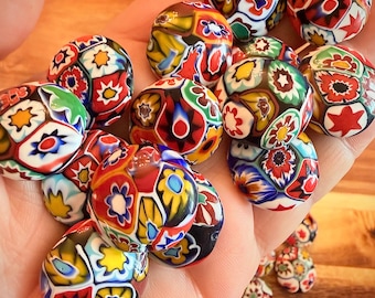 May include: A collection of round glass beads featuring intricate millefiori patterns in vibrant colors including red, yellow, blue, green, and white. Each bead displays a unique mosaic of floral and star-like shapes across its surface.