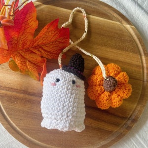 Puede incluir: Un fantasma de crochet con un sombrero de copa negro y una calabaza naranja de crochet. El fantasma y la calabaza est&aacute;n conectados por una cuerda blanca.