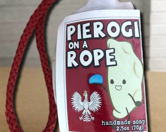Puede incluir: Una pastilla de jabón artesanal en una cuerda roja, etiquetada Pierogi on a Rope. La etiqueta blanca presenta un pierogi de dibujos animados, un emblema de águila polaca y el texto 2.5oz (70g). El jabón tiene forma de pierogi y cuelga de un cordón rojo.