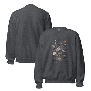 May include: A dark heather gray crewneck sweatshirt featuring a graphic print of wildflowers, a crescent moon, and a butterfly. The text "ADVENTURE FOUND HER AGAIN" is printed below the floral design. The sweatshirt is shown from both front and back.
