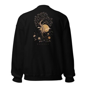 May include: A black crewneck sweatshirt featuring a graphic on the back. The design displays a tree with exposed roots, a large circular moon, and various flowers in shades of beige and brown. The word ROOTED is printed below the illustration.