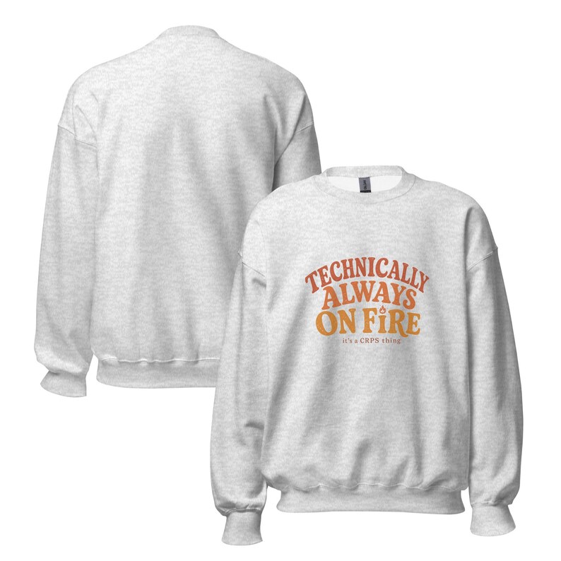 May include: A light gray heather crewneck sweatshirt featuring the orange and yellow text "TECHNICALLY ALWAYS ON FIRE" with a small flame icon above the word "ON" and the smaller text "it's a CRPS thing" printed below the main graphic.