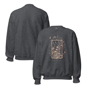 May include: A dark heather gray crewneck sweatshirt featuring a rectangular frame graphic containing a crescent moon, wildflowers, and butterflies. The text "LOVED BEYOND MEASURE" is printed in small letters beneath the floral illustration.