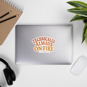 Peut inclure: Un autocollant d&eacute;coup&eacute; pr&eacute;sentant le texte "TECHNICALLY ALWAYS ON FIRE" dans une police orange audacieuse de style r&eacute;tro, avec une petite ic&ocirc;ne de flamme au-dessus de la lettre I. En dessous, le texte "it's a CRPS thing" est &eacute;crit en blanc.