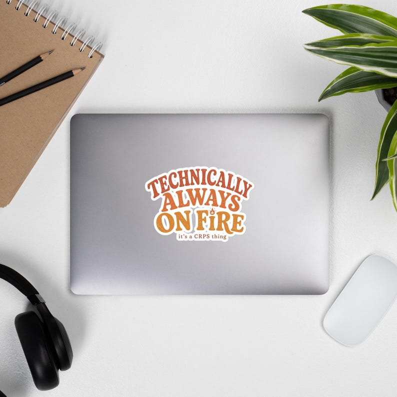 Peut inclure: Un autocollant d&eacute;coup&eacute; pr&eacute;sentant le texte "TECHNICALLY ALWAYS ON FIRE" dans une police orange audacieuse de style r&eacute;tro, avec une petite ic&ocirc;ne de flamme au-dessus de la lettre I. En dessous, le texte "it's a CRPS thing" est &eacute;crit en blanc.