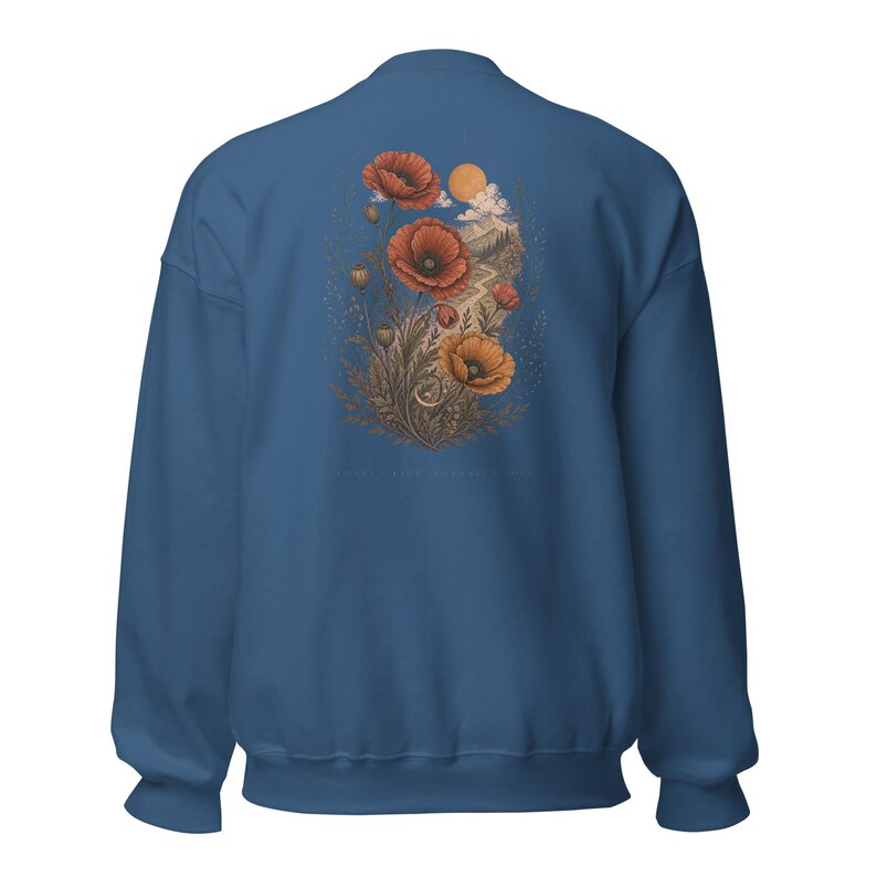 May include: A blue crewneck sweatshirt featuring a back graphic of red and orange poppy flowers, a winding path, mountains, and a sun. The illustration includes fine line details and muted earth tones, centered on the back of the garment.