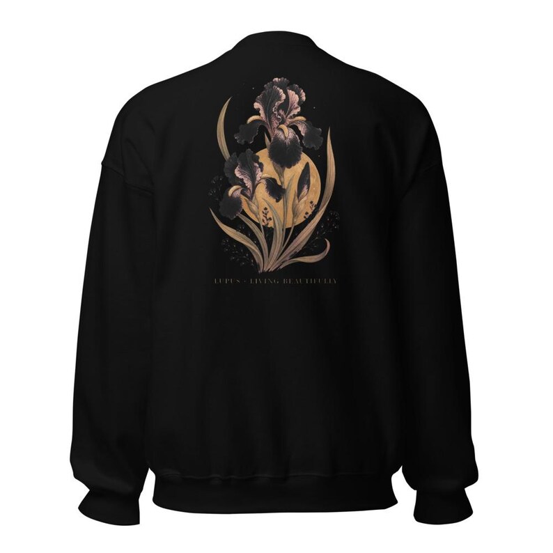 May include: A black long-sleeve sweatshirt featuring a graphic on the back of dark purple iris flowers layered over a large golden yellow circle. Below the floral design, the text reads LUPUS - LIVING BEAUTIFULLY in a small, clean font.