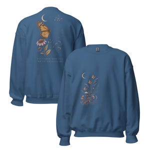 May include: A blue crewneck sweatshirt featuring a back graphic of a monarch butterfly, a flower, a crescent moon, and the text "INVISIBLE DOESN'T MEAN IMAGINARY." The front features a smaller graphic of butterflies, a crescent moon, and floral stems.