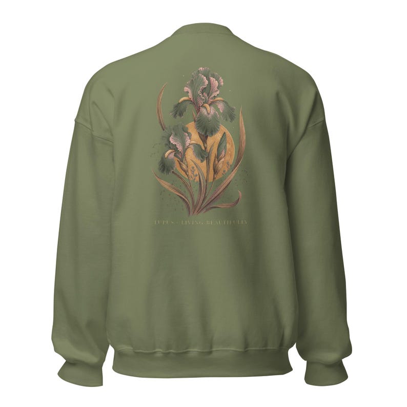May include: An olive green sweatshirt featuring a back graphic of a detailed iris flower in shades of muted pink and green, layered over a golden yellow circle. The text "IRIS - LIVING BEAUTIFULLY" is printed in small, light-coloured capital letters.