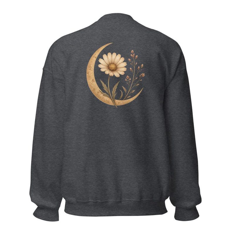 May include: A dark charcoal gray long-sleeve sweatshirt featuring a graphic on the back. The design displays a large, textured golden crescent moon cradling a single blooming daisy flower and a delicate sprig of small wildflowers and buds.