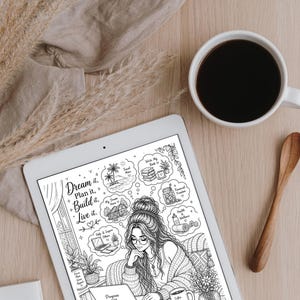 Peut inclure: Une tablette blanche affichant une illustration en noir et blanc d'une femme avec le texte "Dream it, Plan it, Build it, Live it." Une tasse de caf&eacute; et une cuill&egrave;re en bois sont pos&eacute;es sur une surface en bois clair. Des plantes s&eacute;ch&eacute;es et un tissu beige sont &eacute;galement pr&eacute;sents.