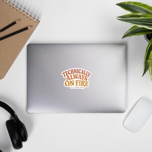 Peut inclure: Un autocollant d&eacute;coup&eacute; pr&eacute;sentant le texte "TECHNICALLY ALWAYS ON FIRE" dans une police orange audacieuse de style r&eacute;tro, avec le texte plus petit "it's a CRPS thing" en dessous. L'autocollant a une bordure blanche et est centr&eacute; sur un ordinateur portable.