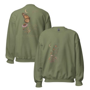 May include: An olive green crewneck sweatshirt featuring a graphic of a monarch butterfly, a crescent moon, and flowers on the back with the text "INVISIBLE DOESN'T MEAN IMAGINARY," and a smaller matching floral and butterfly graphic on the front chest.