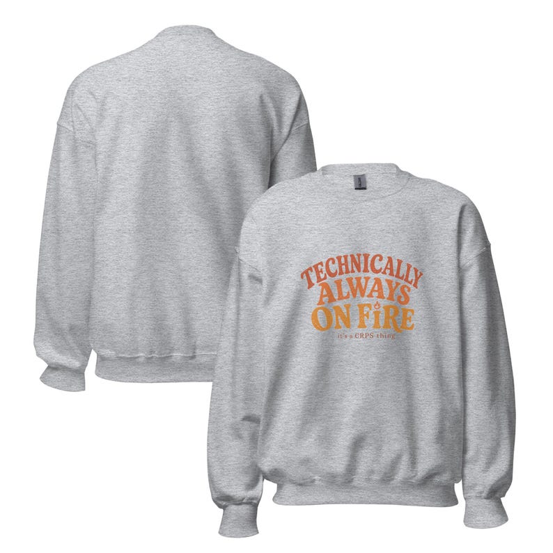 May include: A light grey crewneck sweatshirt featuring the orange text "TECHNICALLY ALWAYS ON FIRE" and "it's a CRPS thing" printed on the front. The garment has long sleeves, a ribbed collar, cuffs, and hem, shown from both front and back views.