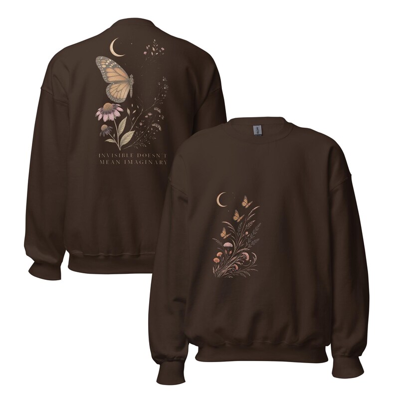 May include: A dark brown crewneck sweatshirt featuring a graphic of a butterfly, flowers, and a crescent moon. The back displays the text "INVISIBLE DOESN'T MEAN IMAGINARY" alongside a butterfly and floral design, while the front shows a smaller floral motif.