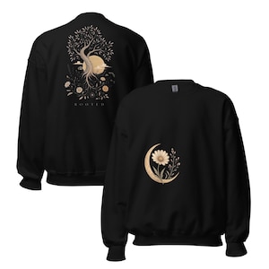 May include: A black crewneck sweatshirt featuring a graphic on the back of a tree with exposed roots, a large moon, and the text "ROOTED" below. The front of the sweatshirt displays a smaller graphic of a single daisy flower inside a crescent moon.