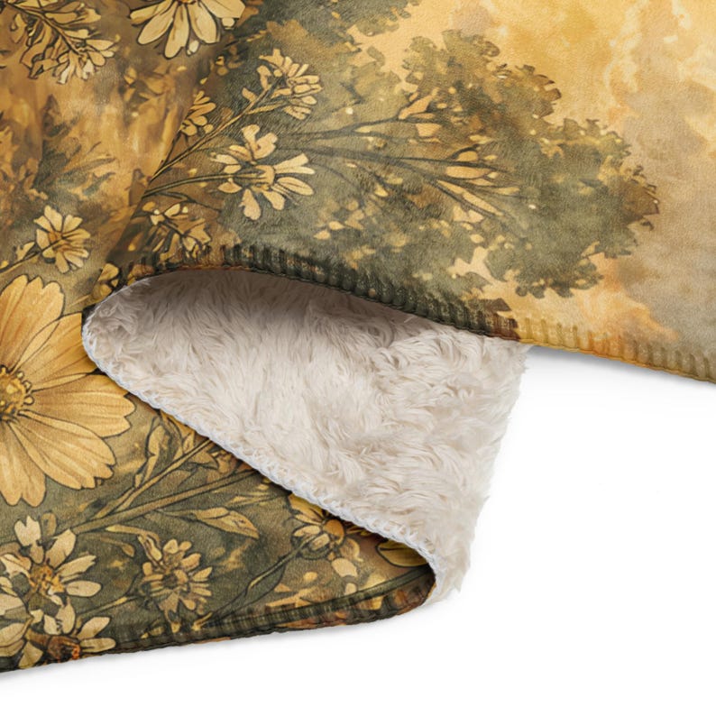 May include: A folded throw blanket featuring a printed pattern of yellow and brown wildflowers against a dark green background. The blanket has a soft, cream-colored faux sheepskin lining visible on the underside where the fabric is folded over.