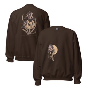 May include: A dark brown crewneck sweatshirt featuring a graphic of a dark purple iris flower layered over a pale yellow moon. The back of the sweatshirt displays a larger version of the same floral design with the text LUDEN - IRISAS DE FICATA.