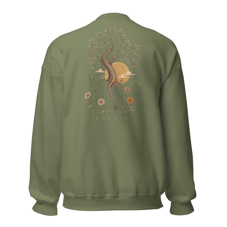 May include: An olive green crewneck sweatshirt featuring a back graphic of a tree with exposed roots, a large yellow sun, clouds, and various wildflowers. The word ROOTED is printed in small, light-colored capital letters below the illustration.