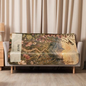 May include: A rectangular throw blanket featuring a detailed nature scene with mountains, wildflowers, and two small birds. A vertical cream-colored panel on the left side displays the text "Beside You Still" in a dark, elegant script font.