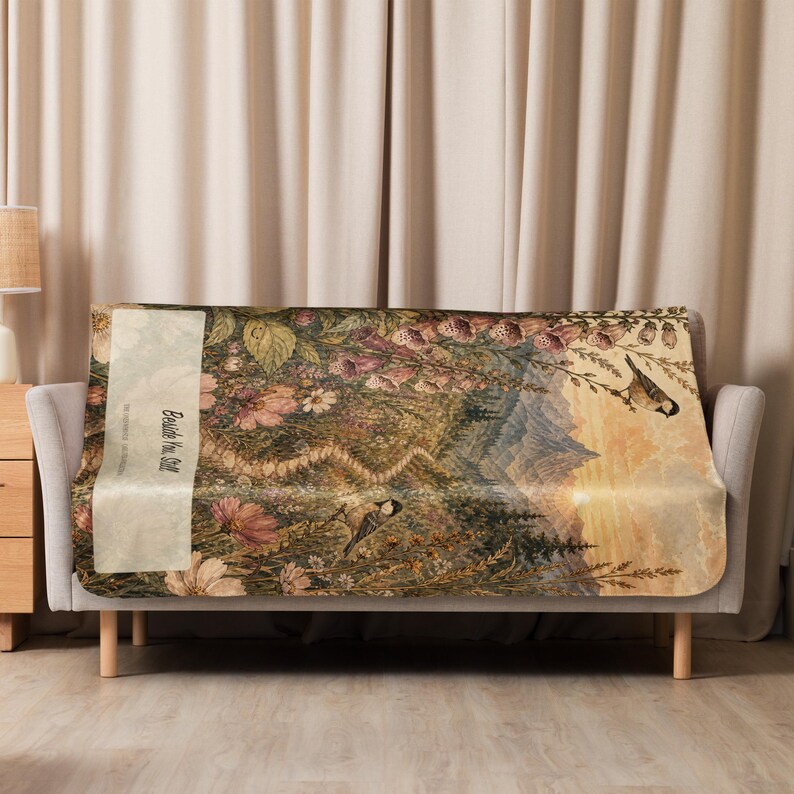 May include: A rectangular throw blanket featuring a detailed nature scene with mountains, wildflowers, and two small birds. A vertical cream-colored panel on the left side displays the text "Beside You Still" in a dark, elegant script font.