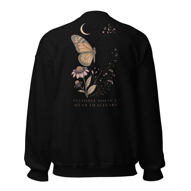 May include: A black long-sleeve sweatshirt featuring a graphic on the back. The design includes a monarch butterfly, a crescent moon, and floral elements in muted tones. Below the illustration, the text reads: INVISIBLE DOESN'T MEAN IMAGINARY.