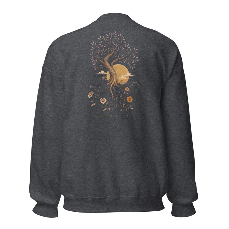 May include: A dark charcoal gray crewneck sweatshirt featuring a graphic on the back. The design depicts a tree with exposed roots, a large yellow sun, clouds, and various flowers. The word ROOTED is printed in small capital letters below the graphic.
