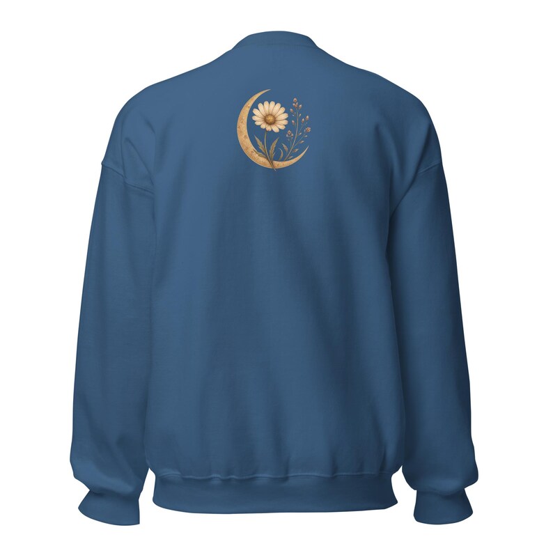 May include: A solid dark blue crewneck sweatshirt featuring a graphic on the upper back. The design depicts a golden crescent moon cradling a single daisy flower with delicate stems and small leaves, rendered in a soft, muted gold color palette.