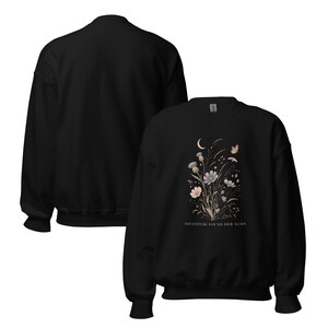 May include: A black crewneck sweatshirt featuring a graphic print of a floral bouquet with a crescent moon and a butterfly. The text ADVENTURE FOUND HER AGAIN is printed in white below the flowers. The design is centered on the front of the garment.