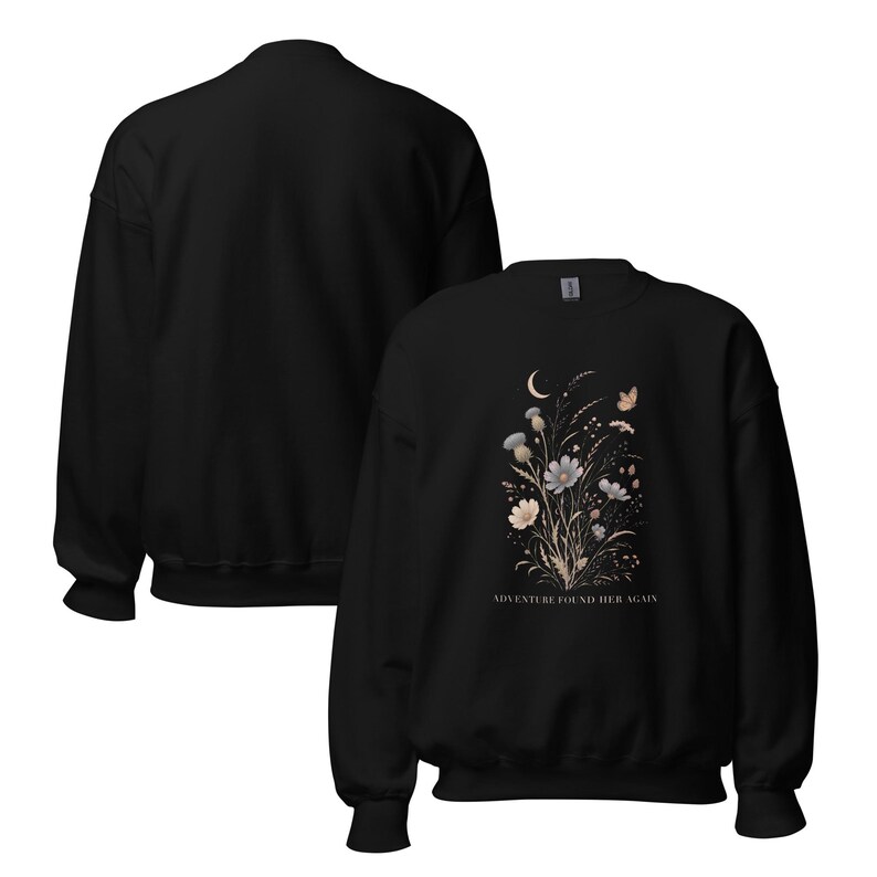 May include: A black crewneck sweatshirt featuring a graphic print of a floral bouquet with a crescent moon and a butterfly. The text ADVENTURE FOUND HER AGAIN is printed in white below the flowers. The design is centered on the front of the garment.