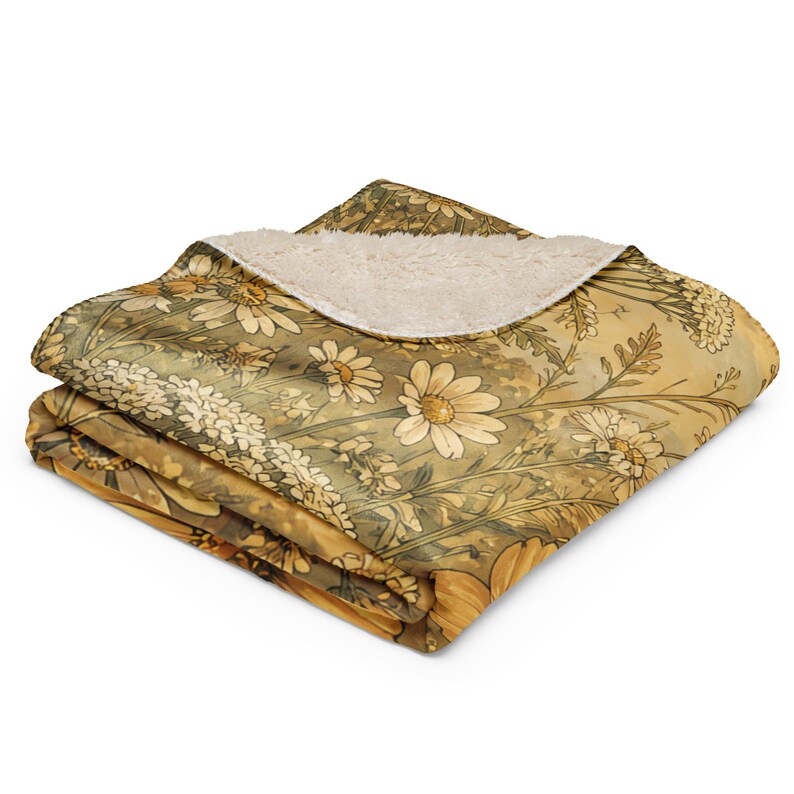 May include: A folded throw blanket featuring a printed pattern of yellow and white daisies on a muted golden-brown background. The blanket has a textured, cream-colored sherpa fleece lining visible on the folded top corner of the fabric.