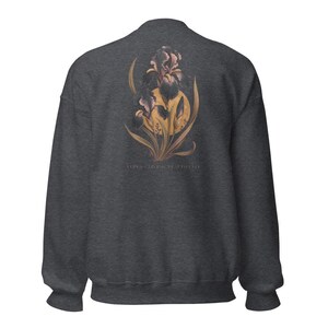 May include: A dark charcoal grey crewneck sweatshirt featuring a graphic on the back. The design displays a large, detailed purple and dark-toned iris flower layered over a golden yellow circular sun, with the text "IRIS - LIVING BEAUTIFULLY" below.