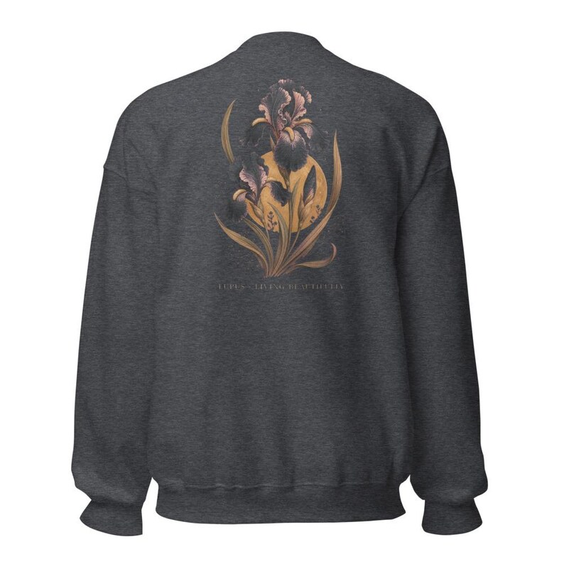 May include: A dark charcoal grey crewneck sweatshirt featuring a graphic on the back. The design displays a large, detailed purple and dark-toned iris flower layered over a golden yellow circular sun, with the text "IRIS - LIVING BEAUTIFULLY" below.
