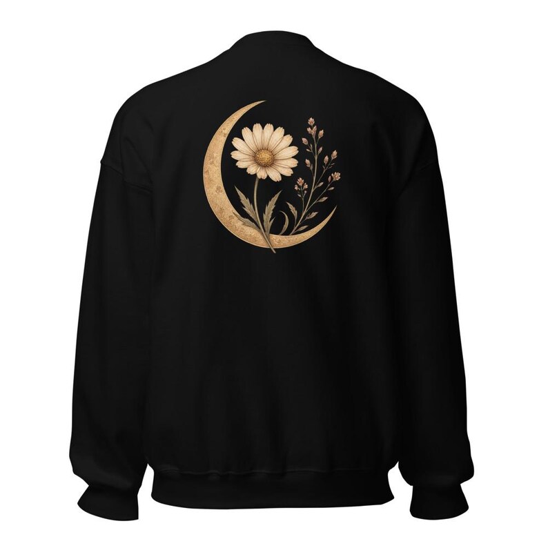 May include: A black long-sleeve sweatshirt featuring a graphic on the back. The design displays a large, textured golden crescent moon cradling a single white daisy flower and a small sprig of delicate wildflowers with tiny buds and leaves.