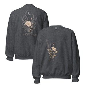 May include: A dark charcoal gray crewneck sweatshirt featuring a botanical illustration of flowers and a crescent moon. The back displays the text "FIBROMYALGIA SOFTLY UNBROKEN" below the floral design, while the front shows a smaller floral graphic.