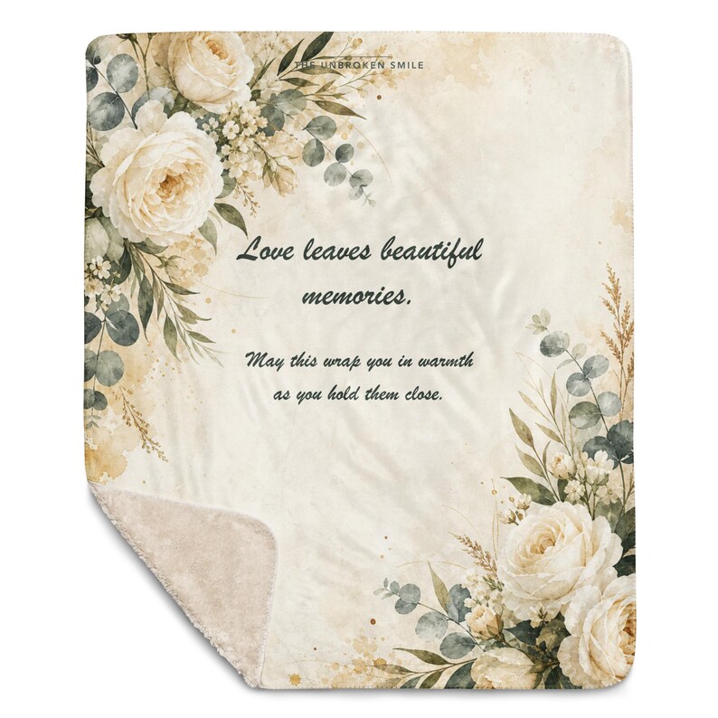 May include: A rectangular throw blanket with a cream-colored background featuring watercolor-style illustrations of white roses and eucalyptus leaves. The text reads: Love leaves beautiful memories. May this wrap you in warmth as you hold them close.