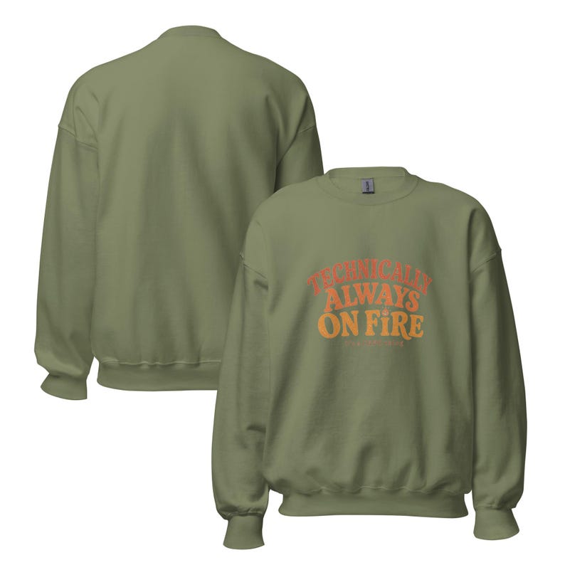 May include: An olive green crewneck sweatshirt featuring the text "TECHNICALLY ALWAYS ON FIRE" printed in a curved, layered orange and red font on the front. The garment has long sleeves with ribbed cuffs and a ribbed hem, shown from both front and back.