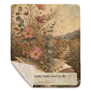 K&ouml;nnte beinhalten: Eine rechteckige Wohndecke mit Sherpa-Fleece-R&uuml;ckseite, die eine Illustration im Vintage-Stil eines aufgeschlagenen Buches mit rosa Bl&uuml;ten und Eukalyptusbl&auml;ttern, einem steinernen Pfad, Bergen und dem Text "This Chapter Looks Good on Me" zeigt.