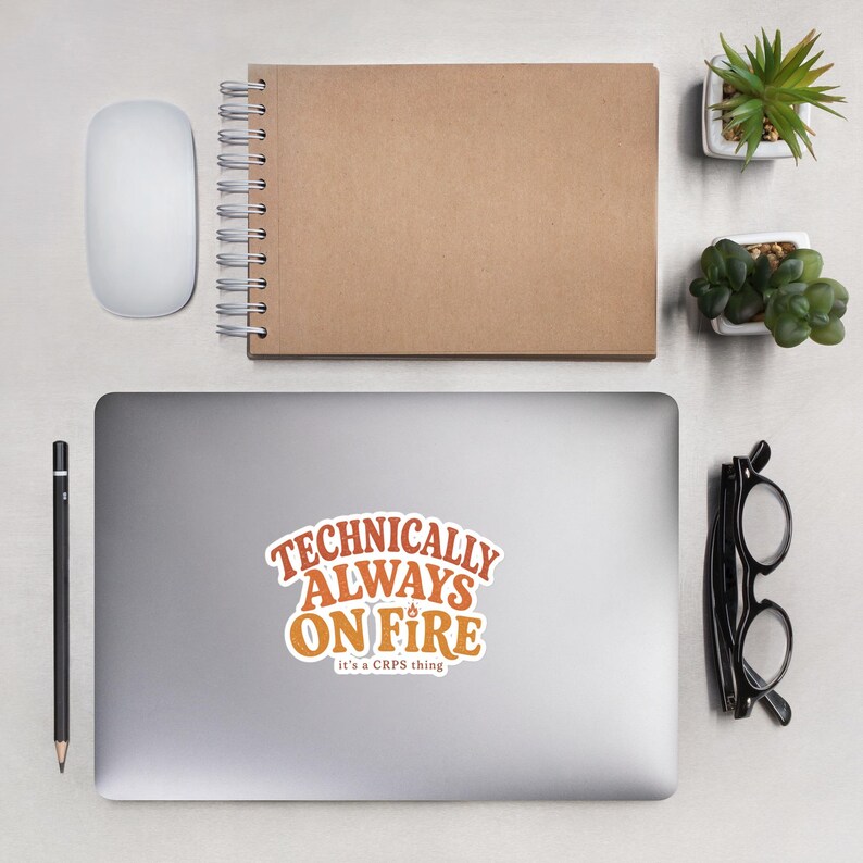 Peut inclure: Un autocollant d&eacute;coup&eacute; pr&eacute;sentant le texte "TECHNICALLY ALWAYS ON FIRE" dans une police orange audacieuse de style r&eacute;tro, avec le texte blanc plus petit "it's a CRPS thing" en dessous. L'autocollant a une bordure blanche sur un ordinateur portable.