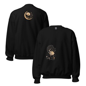May include: A black long-sleeve sweatshirt featuring a graphic on the front of a tree with roots and a sun, and a graphic on the back of a flower inside a crescent moon. The designs are rendered in shades of beige and cream on the black fabric.